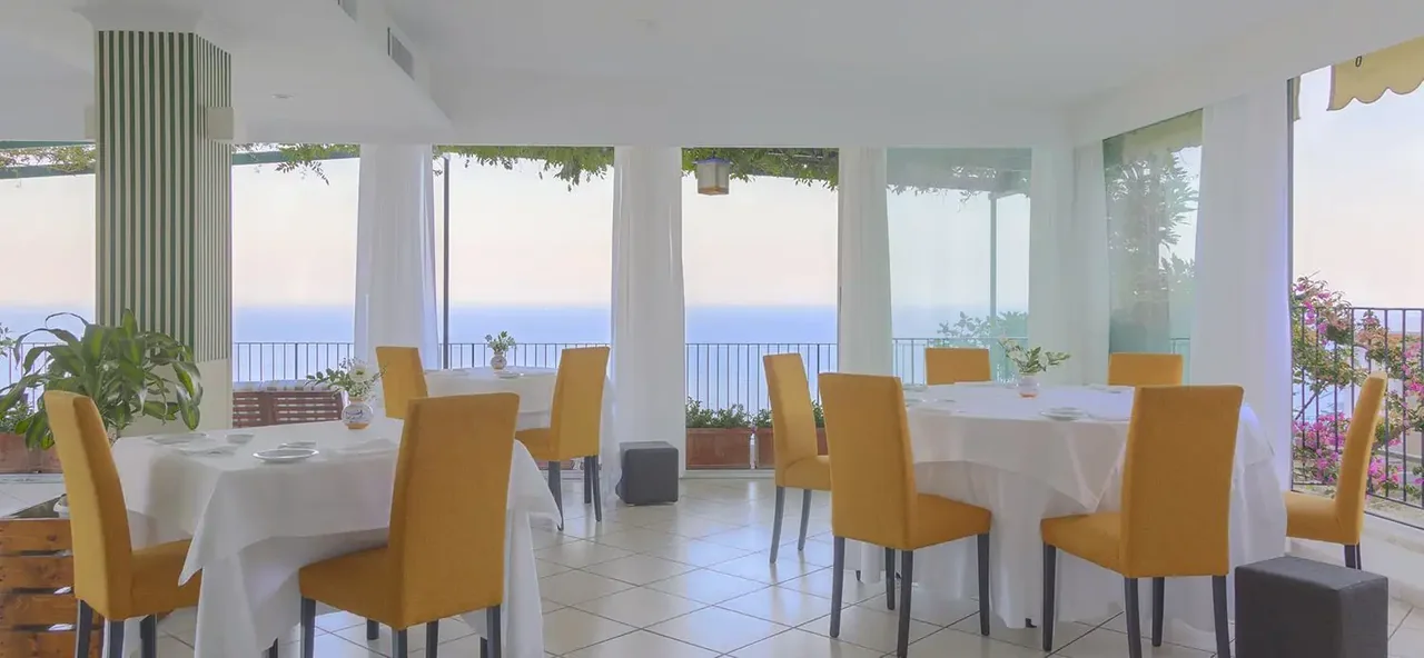 The dining room at Da Ciccio Cielo Mare Terra, with yellow chairs and windows overlooking the sea